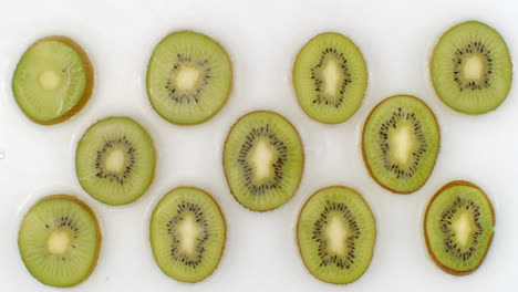 Water-splashes-in-slow-motion.-Top-view:-several-circles-of-kiwi-is-washed-with-water-on-a-white-background.-chopped-fruit.